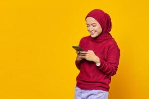 felice giovane donna asiatica che utilizza un telefono cellulare e guarda lo schermo dello smartphone su sfondo giallo foto