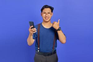 ritratto di allegro giovane uomo asiatico che tiene il telefono cellulare e mostra i pollici in su segno foto