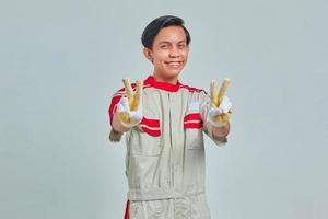 ritratto di allegro bell'uomo che indossa l'uniforme del meccanico che fa segno di pace con le dita su sfondo grigio foto