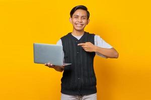 sorridente bel giovane che punta il dito al computer portatile su sfondo giallo foto