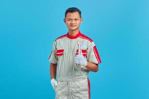 ritratto di giovane meccanico asiatico sorridente che tiene la chiave in mano e guarda la telecamera su sfondo blu foto