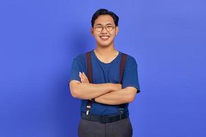 ritratto di giovane uomo asiatico sorridente che incrocia le braccia e indossa occhiali su sfondo viola foto