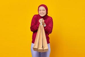 donna asiatica eccitata e sorridente che chiude gli occhi e tiene in mano le borse della spesa su sfondo giallo
