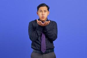 il ritratto di un affascinante giovane uomo asiatico tiene i palmi della mano invia un bacio d'aria su sfondo viola