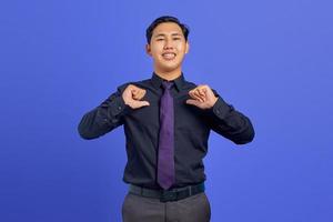 sorridente giovane uomo asiatico che punta a se stessa con orgoglio su sfondo viola foto