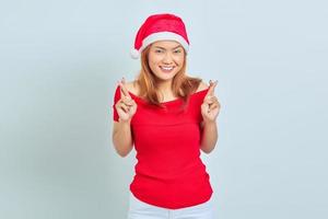 bella giovane donna con i capelli corti che indossa il cappello di Natale sorridendo e gesticolando con le dita incrociate su sfondo bianco foto