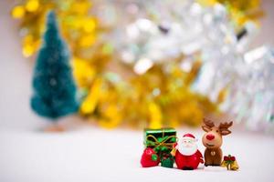 statuine di babbo natale e renne in ceramica o resina su sfondo bianco morbido. sfondo oro e argento con albero di Natale sfocato. confezione regalo verde e campana d'oro. foto