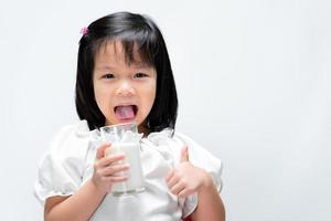 dolce bambino sorridente che tiene il latte di vetro. bambino che mostra i pollici in su significa che è fantastico. bere latte per aumentare il concetto di calcio sano. foto