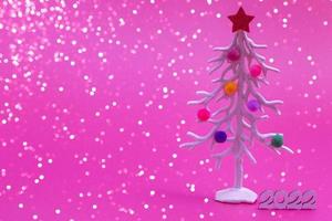 Biglietto natalizio. sullo sfondo delle luci di natale, un albero di natale bianco in giocattoli di pelliccia multicolori con i numeri 2022. primo piano foto