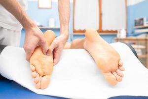 le mani del terapista massaggiano il piede maschile foto