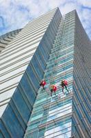 gruppo di specialisti che puliscono la facciata in vetro di un grattacielo, lavori ad alto rischio foto