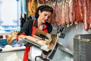 Macellaio femminile che taglia il prosciutto di York in una macchina da taglio foto