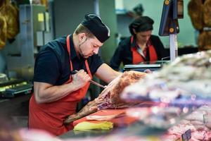 macellai disossare un prosciutto in una moderna macelleria foto