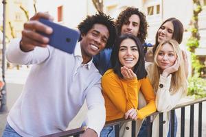 uomo di colore con i capelli afro che si fa un selfie con lo smartphone con il suo gruppo multietnico di amici. foto