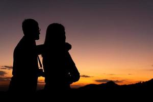 silouette di uomo e donna in coppia che guardano il tramonto dietro la montagna foto