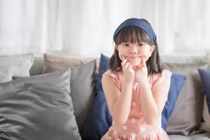 ritratto di una bambina asiatica carina con un sorriso affascinante e felice nel soggiorno di casa. foto