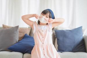 la piccola ragazza asiatica carina che indossa una maschera igienica per prevenire l'epidemia di coronavirus o covid-19 mantiene le distanze sociali e resta a casa. foto