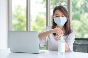 donna d'affari che indossa una maschera e usa un disinfettante personale per pulirsi la mano in ufficio per mantenere l'igiene.preventivo durante il periodo di epidemia da coronavirus o covid19.