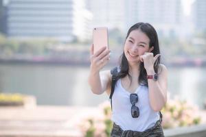 bella donna turistica asiatica che prende selfie su uno smartphone nel centro urbano della città. viaggio di vacanza in estate. foto