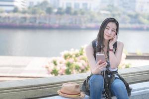 bella donna asiatica turistica solista che si rilassa e si diverte ad ascoltare la musica su uno smartphone nel centro urbano della città. viaggio di vacanza in estate. foto