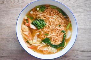 zuppa di noodle wonton maiale giallo noodle con rosso arrosto di maiale gnocco e bog choy verdure cinesi in una ciotola di zuppa sul tavolo di legno, vista dall'alto foto