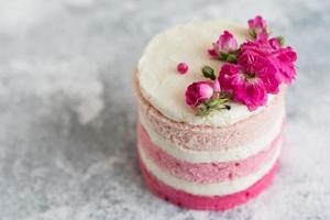 una piccola torta bianca e rosa decorata con fiori e frutti di bosco foto