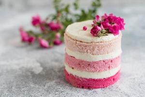 una piccola torta bianca e rosa decorata con fiori e frutti di bosco foto