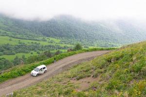 l'auto bianca si trova su una strada sterrata con una donna che cammina fuori in una pittoresca montagna caucasica