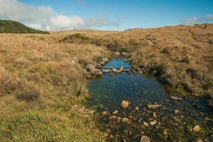 torrente con pietre che attraversa colline ricoperte da cespugli secchi su pianure rurali chiamate pampa vicino a cambara do sul. una piccola cittadina di campagna nel sud del Brasile con incredibili attrazioni turistiche naturali. foto