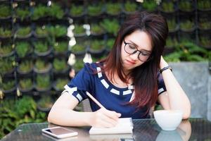 la giovane donna d'affari asiatica tra il lavoro pensante prende nota di qualcosa che fa e l'orologio nel parco estivo o nell'ufficio all'aperto. foto