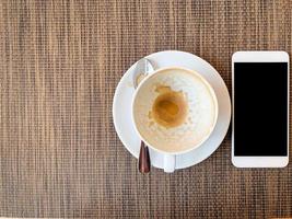 smartphone e tazza di caffè vuota sulla scrivania in legno in vista dall'alto. foto