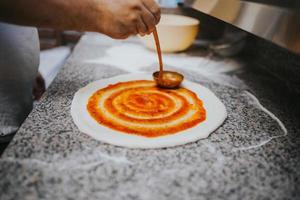 uomo che mette la salsa di pomodoro sull'impasto della pizza foto