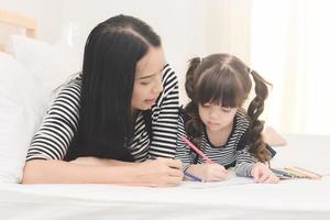 famiglia felice in camera da letto, giovane madre che insegna a sua figlia a studiare a casa. serie di foto di famiglia, bambini e concetto di persone felici.