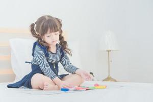 la graziosa bambina asiatica si diverte a giocare con il set di giocattoli mentre è seduta sul letto nella cameretta dei bambini a casa. foto