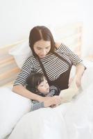 Felice amorevole famiglia giovane madre asiatica che legge un libro di favole da letto a sua figlia in camera da letto.design fotografico per la famiglia, i bambini e il concetto di persone felici foto