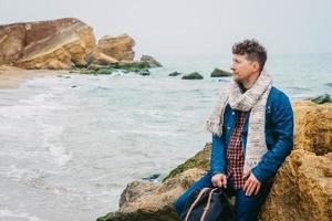 uomo viaggiatore con zaino in piedi sulla spiaggia sabbiosa in mezzo alle rocce sullo sfondo del mare foto