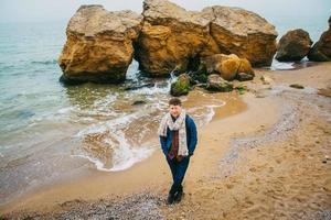 uomo viaggiatore con zaino in piedi sulla spiaggia sabbiosa in mezzo alle rocce sullo sfondo del mare foto