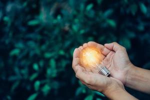 primo piano mano uomo tenere la lampadina su sfondo verde natura foto