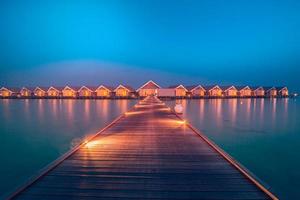 tramonto sull'isola delle maldive, resort di ville sull'acqua di lusso e molo in legno. bel cielo e nuvole e sfondo della spiaggia per le vacanze estive e il concetto di viaggio foto