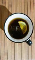 tazza bianca con tè nero e fetta di limone su fondo in legno foto