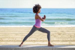 donna nera, acconciatura afro, fare yoga in asana guerriera in spiaggia foto