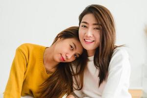 belle giovani donne asiatiche lgbt lesbica coppia felice seduta sul letto abbracciando e sorridendo insieme in camera da letto a casa. lgbt coppia lesbica insieme al chiuso concetto. passare del tempo piacevole a casa. foto