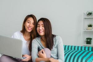 belle giovani donne asiatiche lgbt lesbica coppia felice seduta sul divano acquisto online utilizzando il computer portatile nel soggiorno di casa. lgbt coppia lesbica insieme al chiuso concetto. passare del tempo piacevole a casa. foto