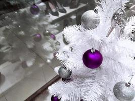 giocattolo viola molto peri su un albero di natale bianco. albero di natale in negozio foto