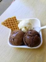 gelato al gusto di cioccolato e waffle modello di dessert congelato in tazza bianca che tiene la mano sul tavolo. foto