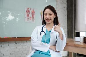 ritratto di bella dottoressa di etnia asiatica in uniforme con stetoscopio, pollice in su, sorridente e guardando la telecamera in una clinica, una persona esperta nel trattamento professionale. foto