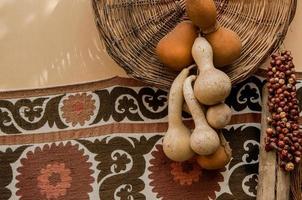 zucca essiccata e vassoio di vimini appesi sullo sfondo del tappeto orientale. decorazione artistica zucca essiccata e tappeto orientale con cesto di vimini foto