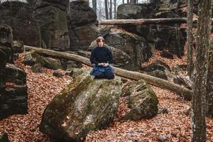 l'uomo in kimono nero con una spada medita e si concentra su rocce e sullo sfondo della foresta foto