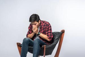 l'uomo con una camicia a righe si siede malato e si siede su una sedia e incrocia le braccia. foto