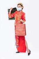 la donna indossa un abito cheongsam sorride con un sacchetto di carta dallo shopping nel capodanno cinese